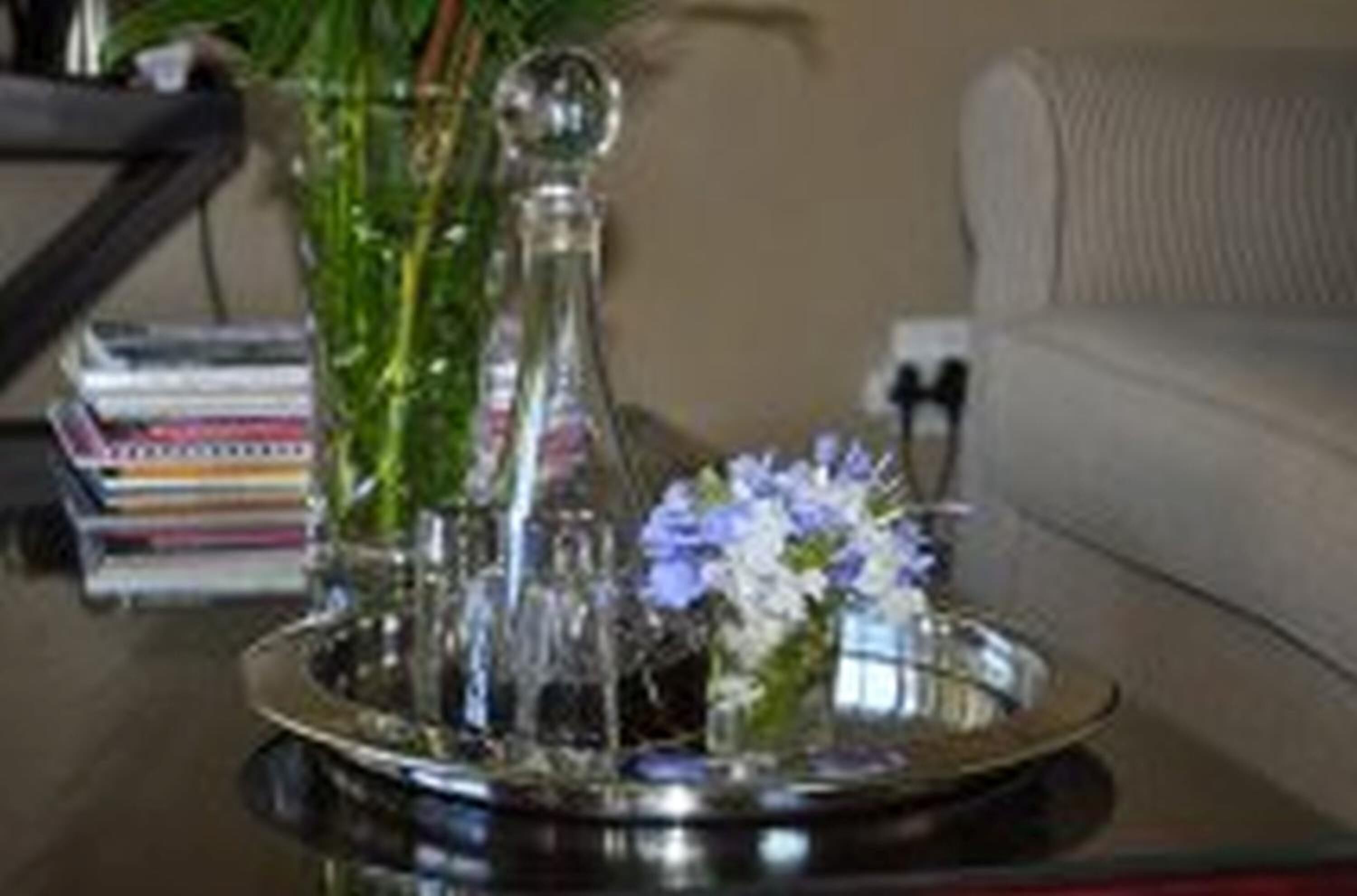 A table with a decorative glass vase containing flowers, a metal tray, and a stack of books.