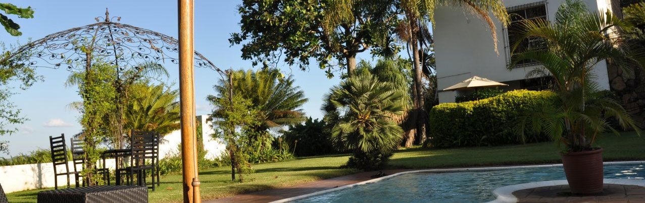Zona junto a la piscina con pérgola, mobiliario exterior y abundante vegetación.