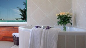 A bathroom with a large bathtub, a window with a view, and a vase with flowers. - Sandra's Guest House (Langebaan)