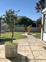 Un patio con un camino empedrado, un árbol pequeño, una maceta grande y una cerca de madera.