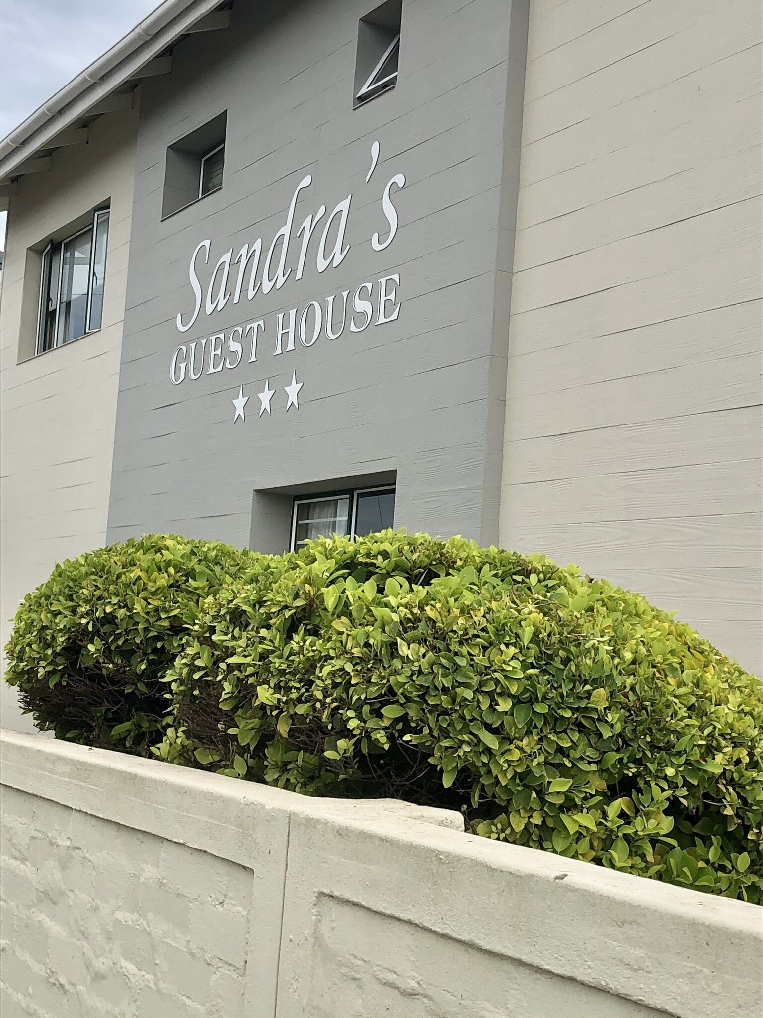 Un edificio con el letrero "Sandra's Guest House" y un seto bien cuidado al frente.