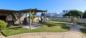 Ein Garten mit Pergola, Gartenmöbeln, einem Grill und einem dekorativen Steinpflanzgefäß.