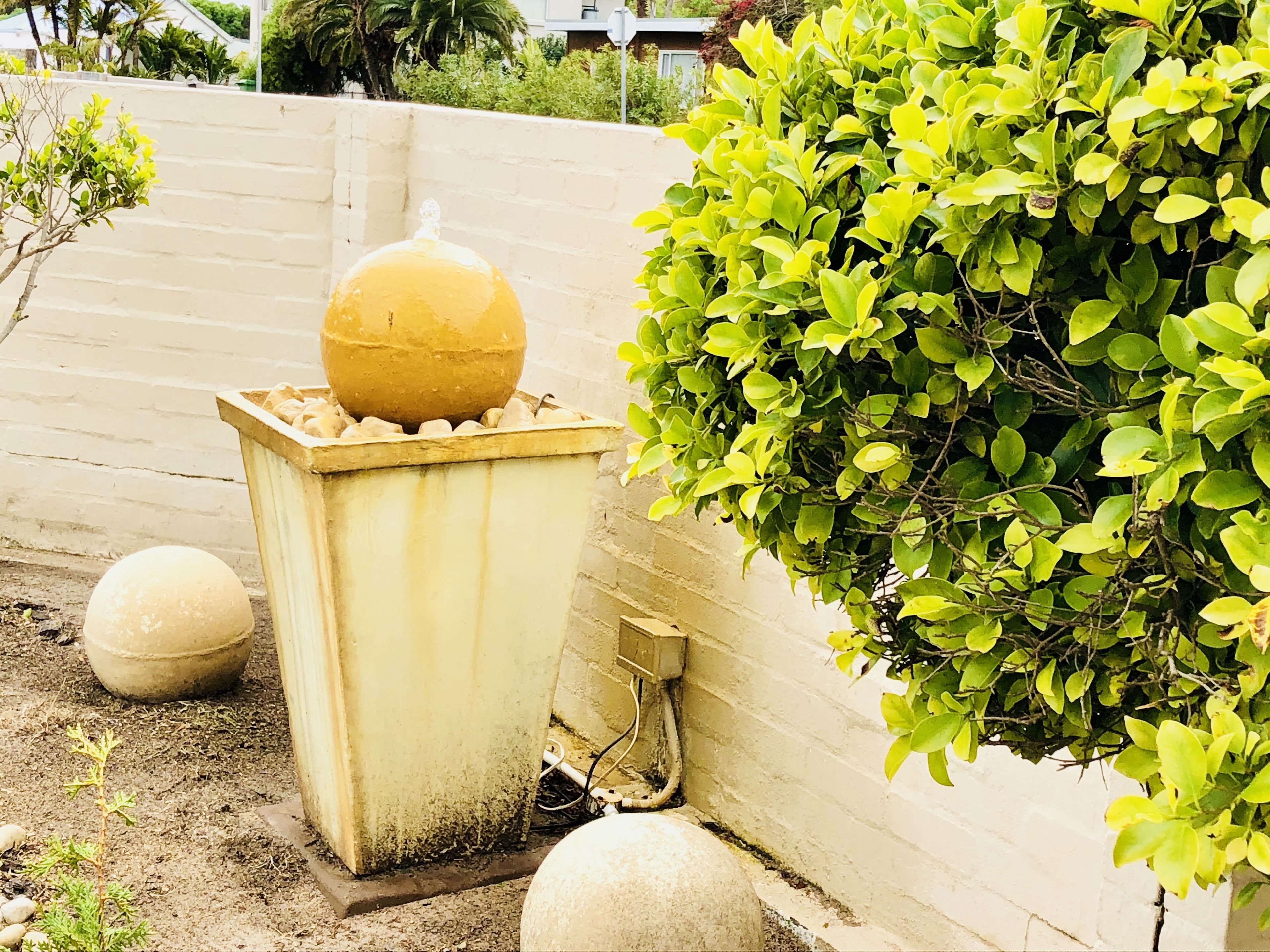 A concrete planter with a yellow spherical object, a white spherical object, and a green bush.
