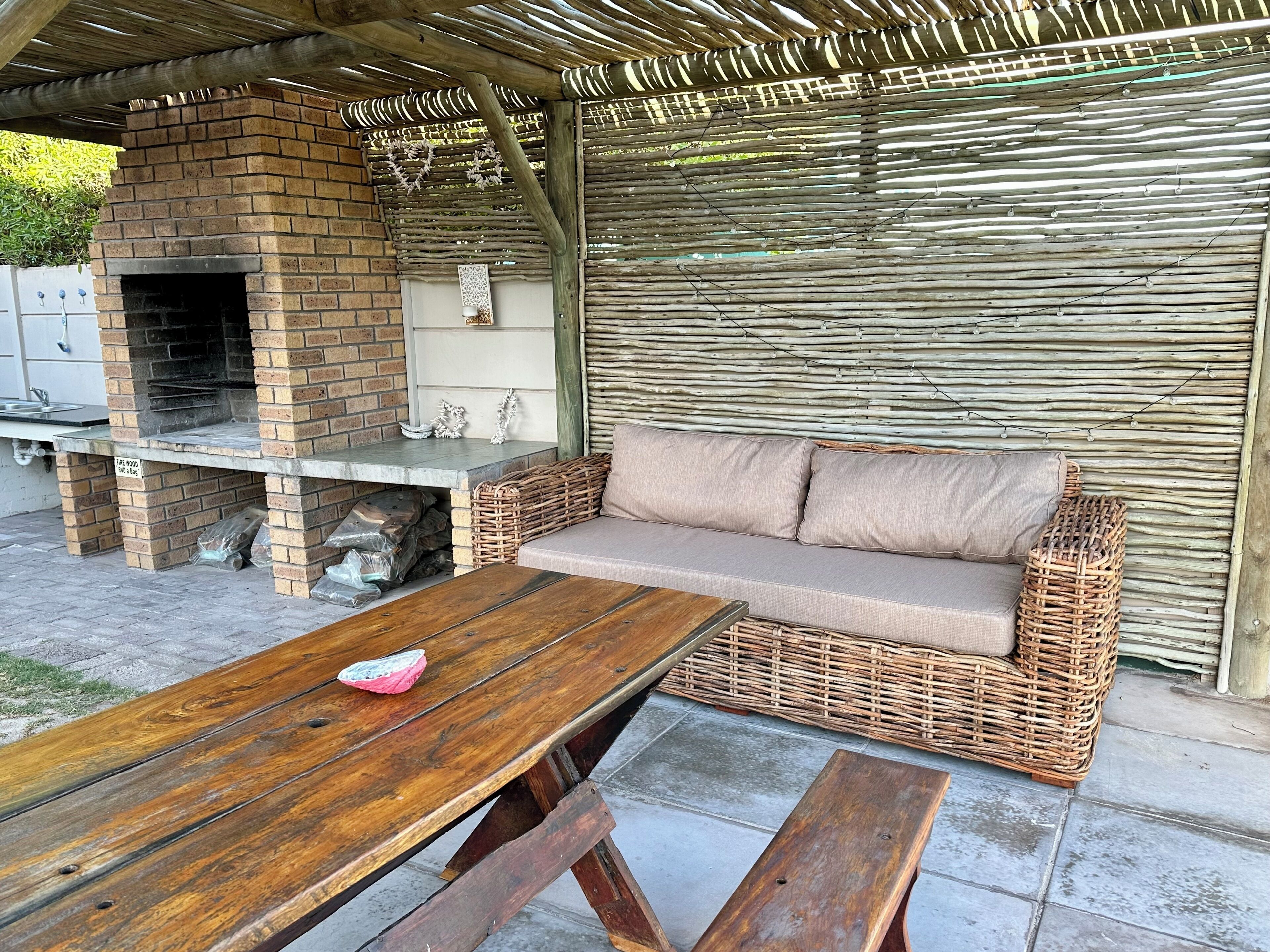 Une terrasse extérieure avec une cheminée en briques, un canapé en osier et une table en bois.