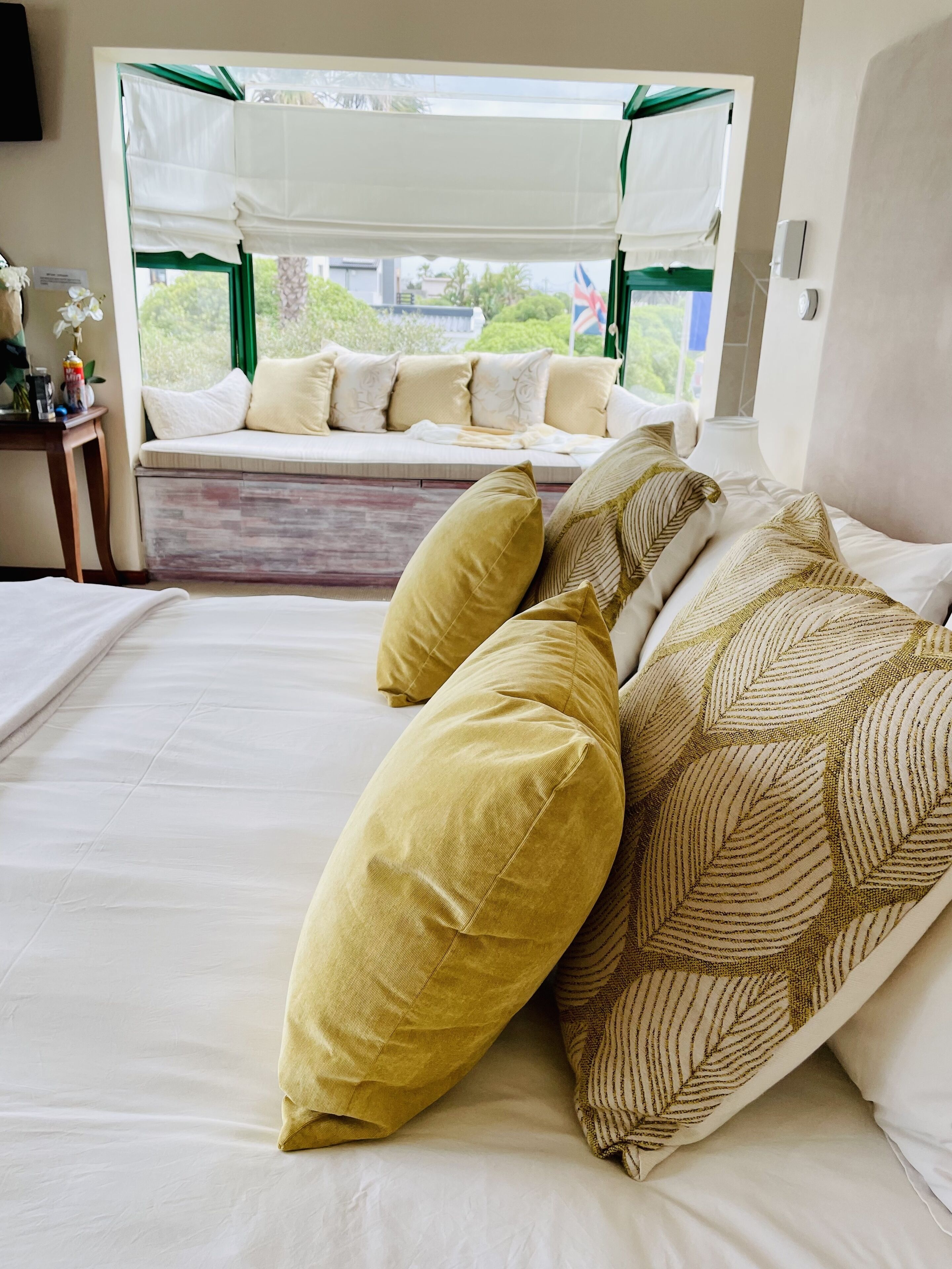 A bedroom with a bed, pillows, a window with a view, and a bedside table.