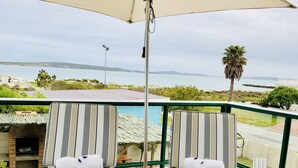 Two striped lounge chairs with towels, an umbrella, and a view of the sea and hills. - Sandra's Guest House (Langebaan)