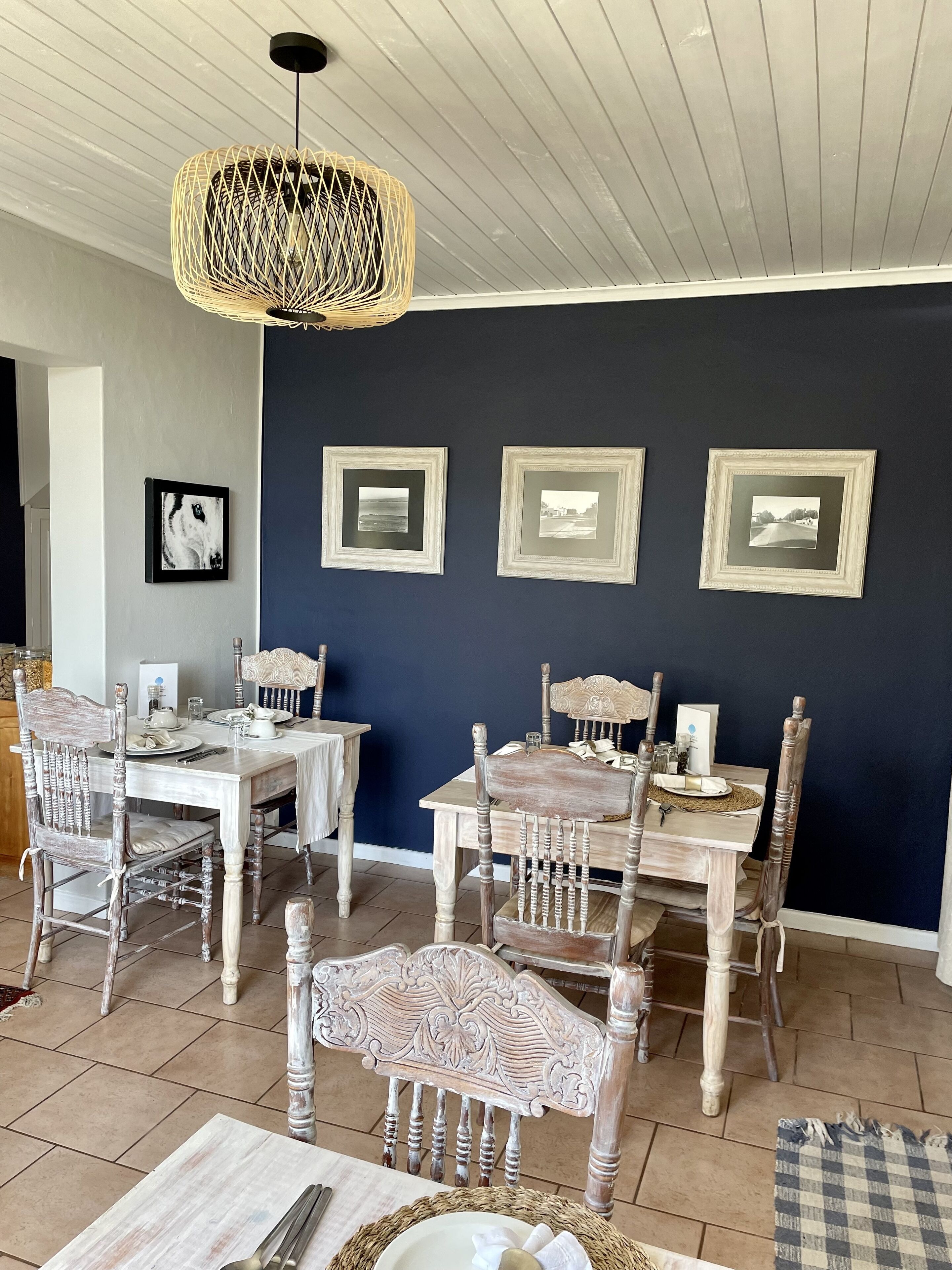 A dining area with a dark blue wall, three framed pictures, and a woven pendant light.