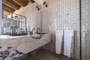 A bathroom with a marble countertop, a sink with a mirror, a shower with a glass door, and a towel rack.