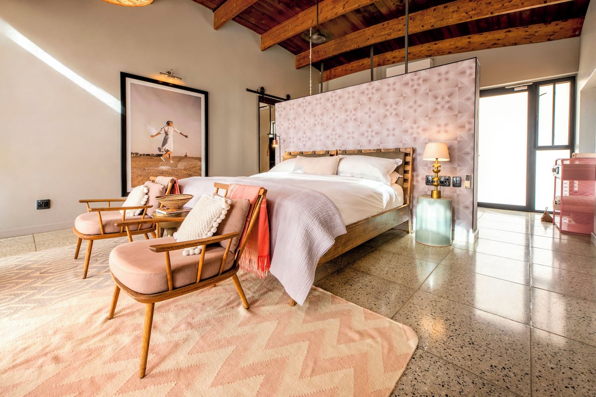 A bedroom with a bed, a chair, a rug, and a wall-mounted lamp.