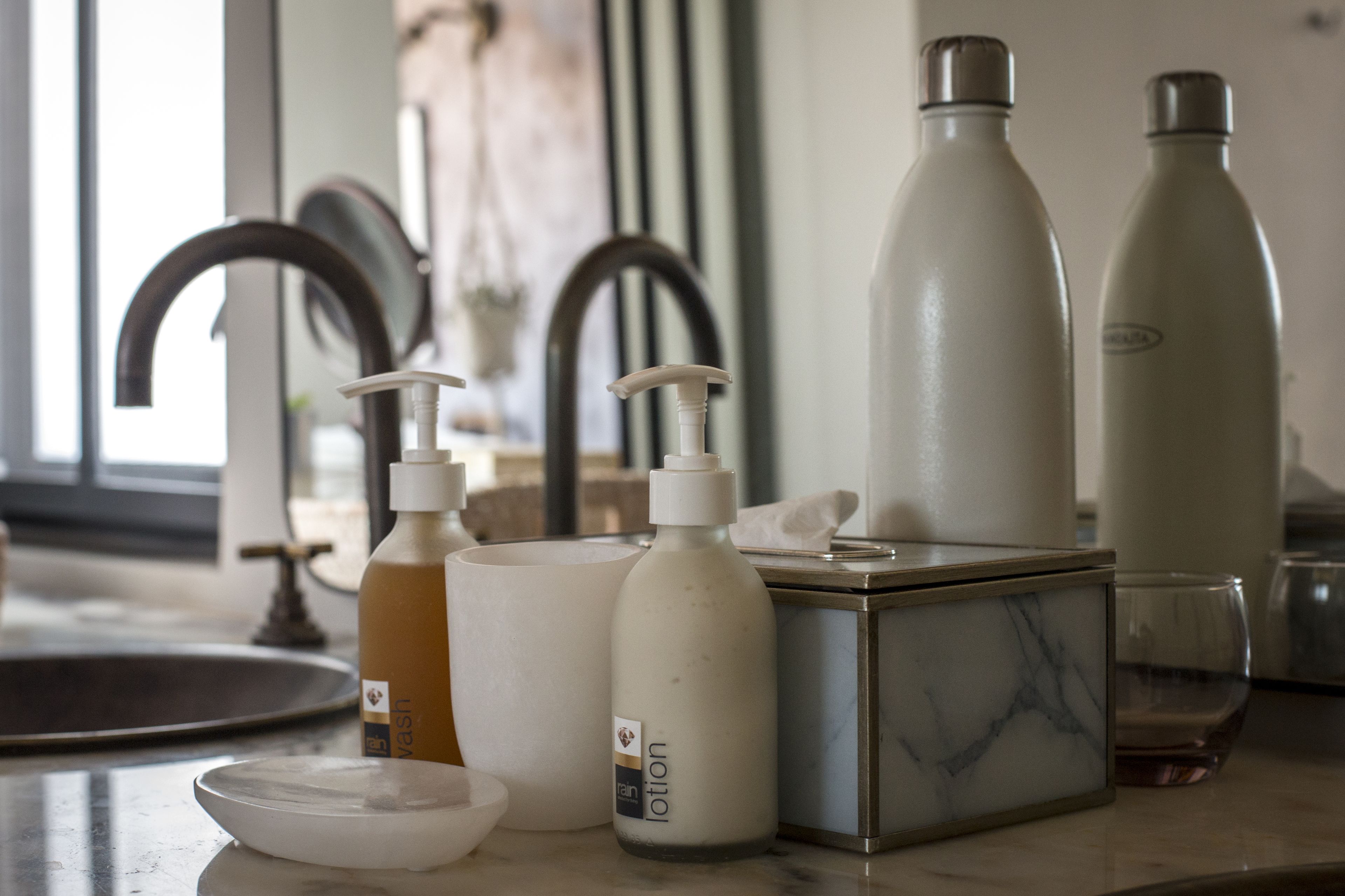 A bathroom counter with a soap dispenser, a lotion bottle, a glass, and a marble box.