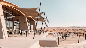 An outdoor dining area with tables and chairs, a covered seating area, and a view of the desert landscape.
