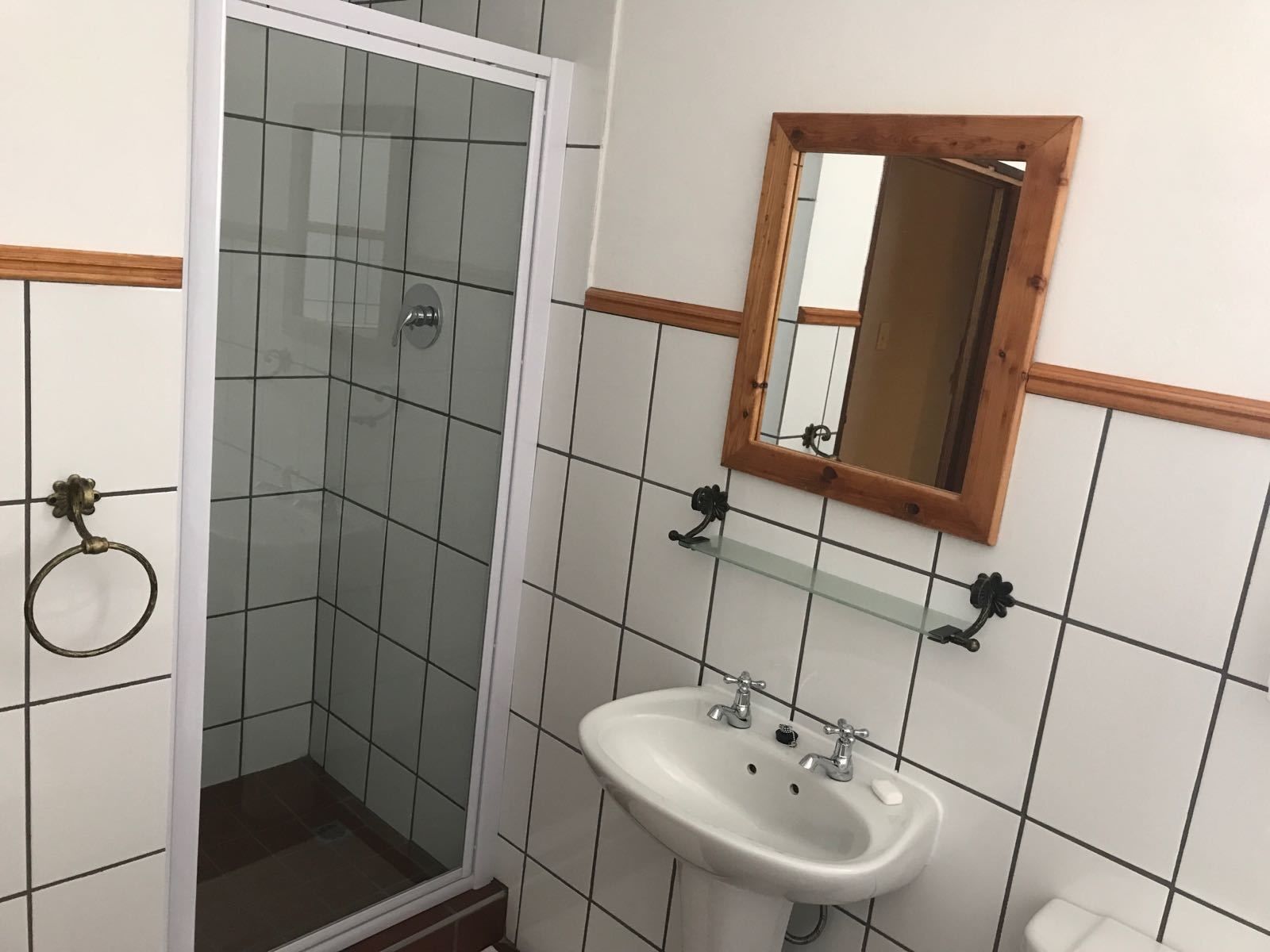 A bathroom with a glass shower enclosure, a white sink with two faucets, and a wooden-framed mirror.