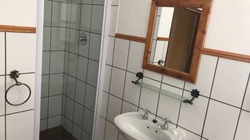 A bathroom with a glass shower enclosure, a white sink with two faucets, and a wooden-framed mirror.