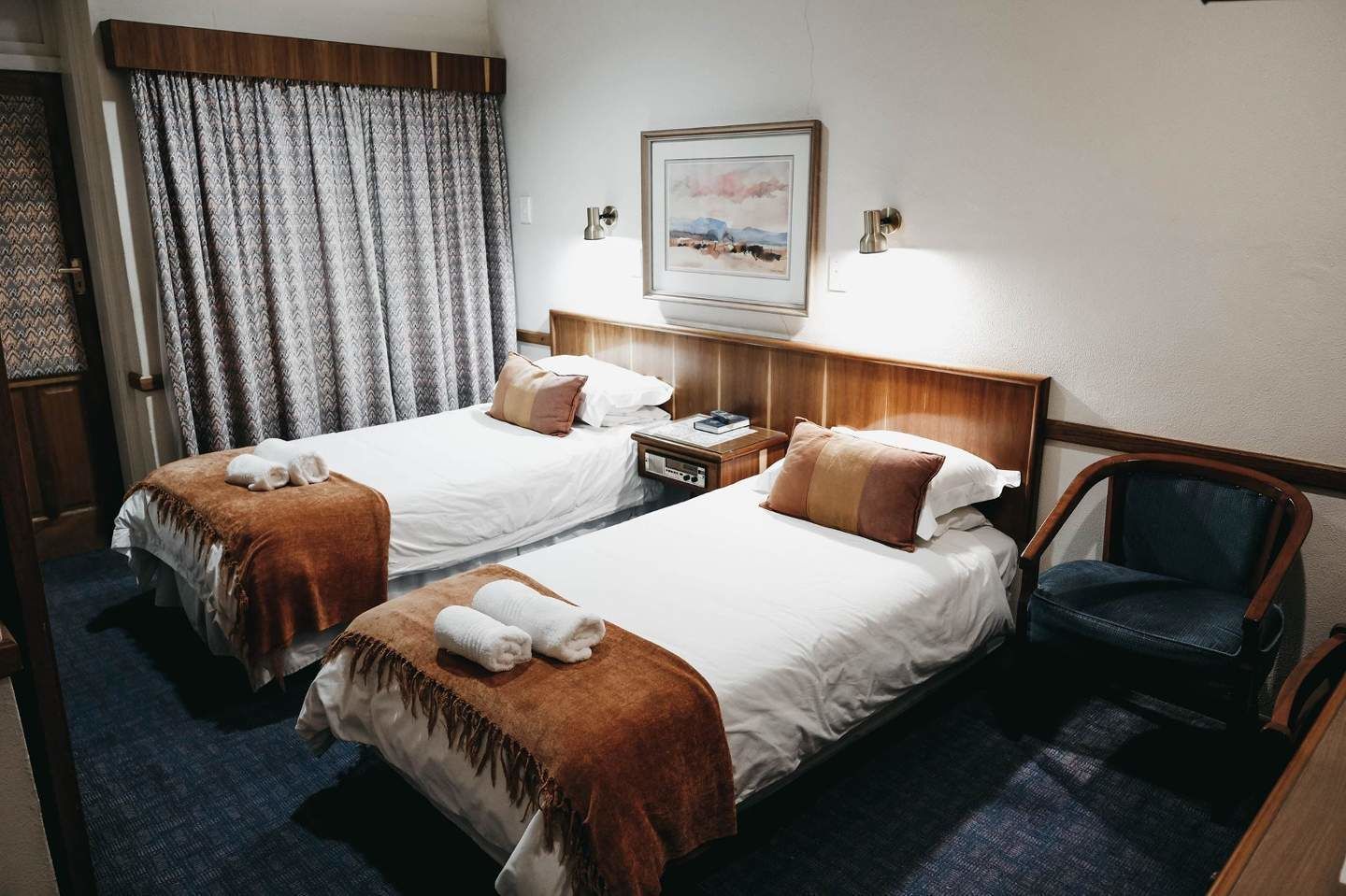 A hotel room with two beds, a nightstand, a chair, and a painting on the wall.