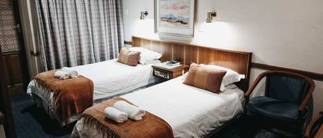 A hotel room with two beds, a nightstand, a chair, and a painting on the wall.
