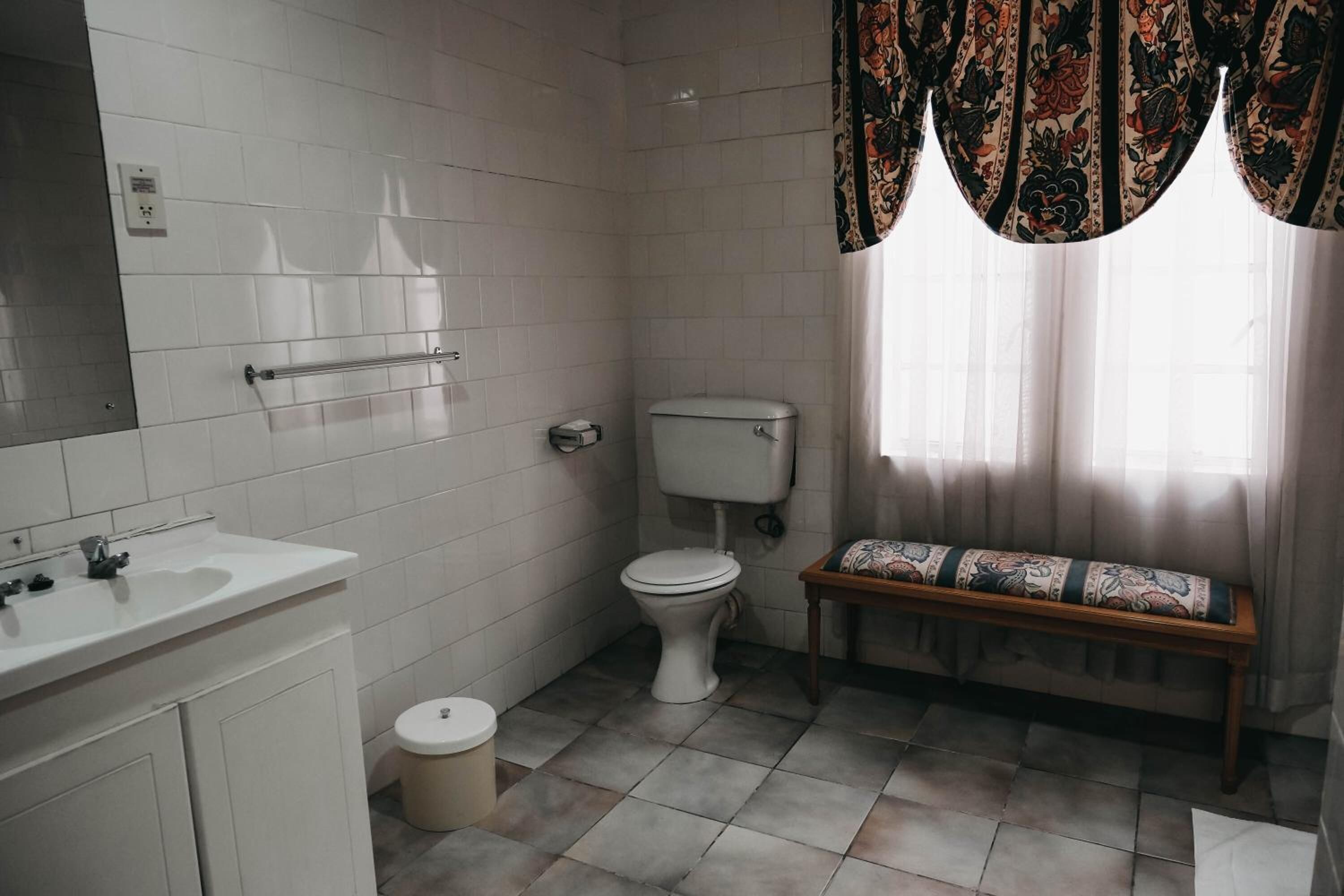 A bathroom with white tiles, a toilet, a sink, and a bench.