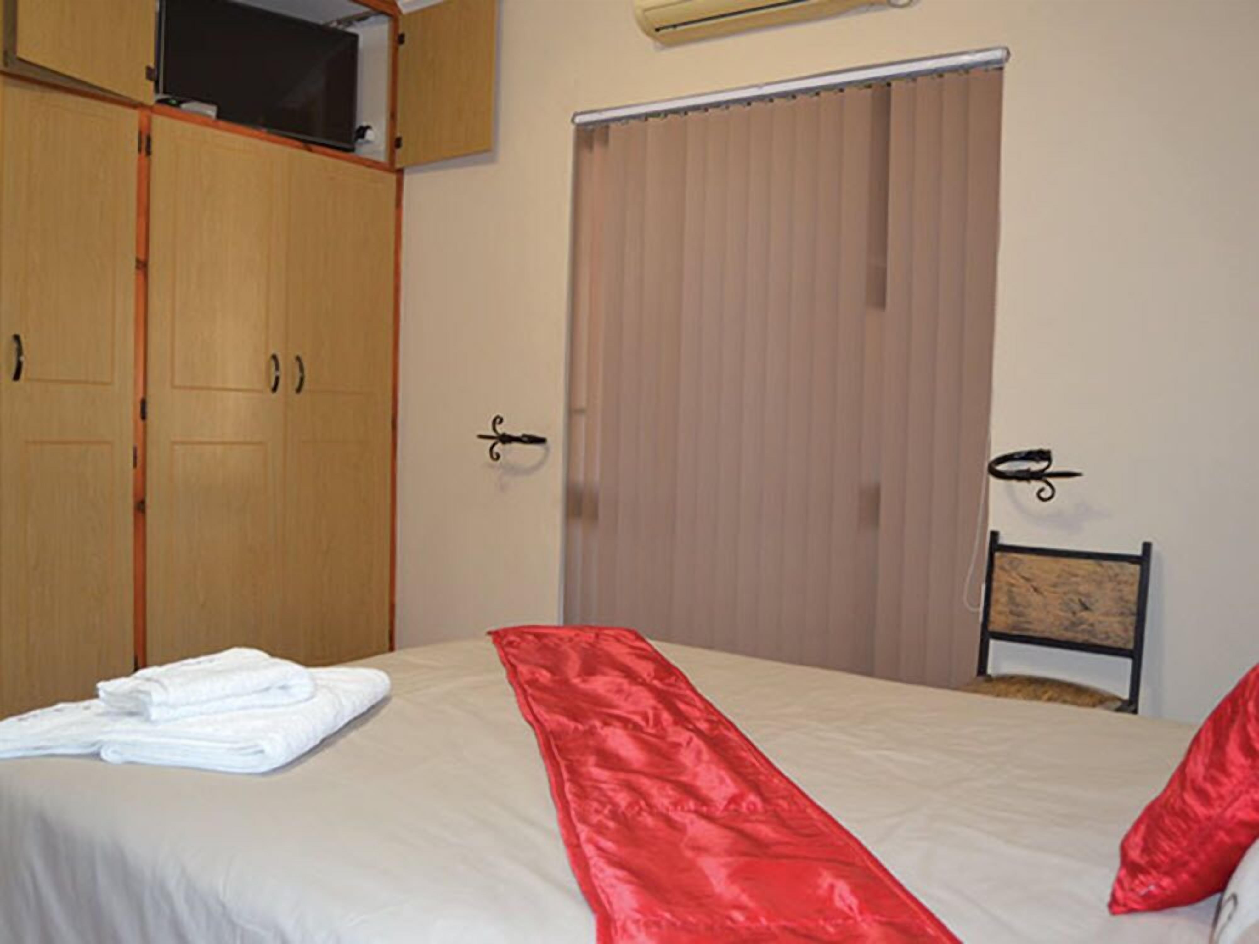 A hotel room with a bed, a wardrobe, a television, and a window with curtains.