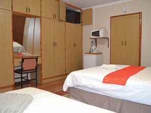 Habitación de hotel con dos camas, un escritorio, una silla, un microondas y un armario.