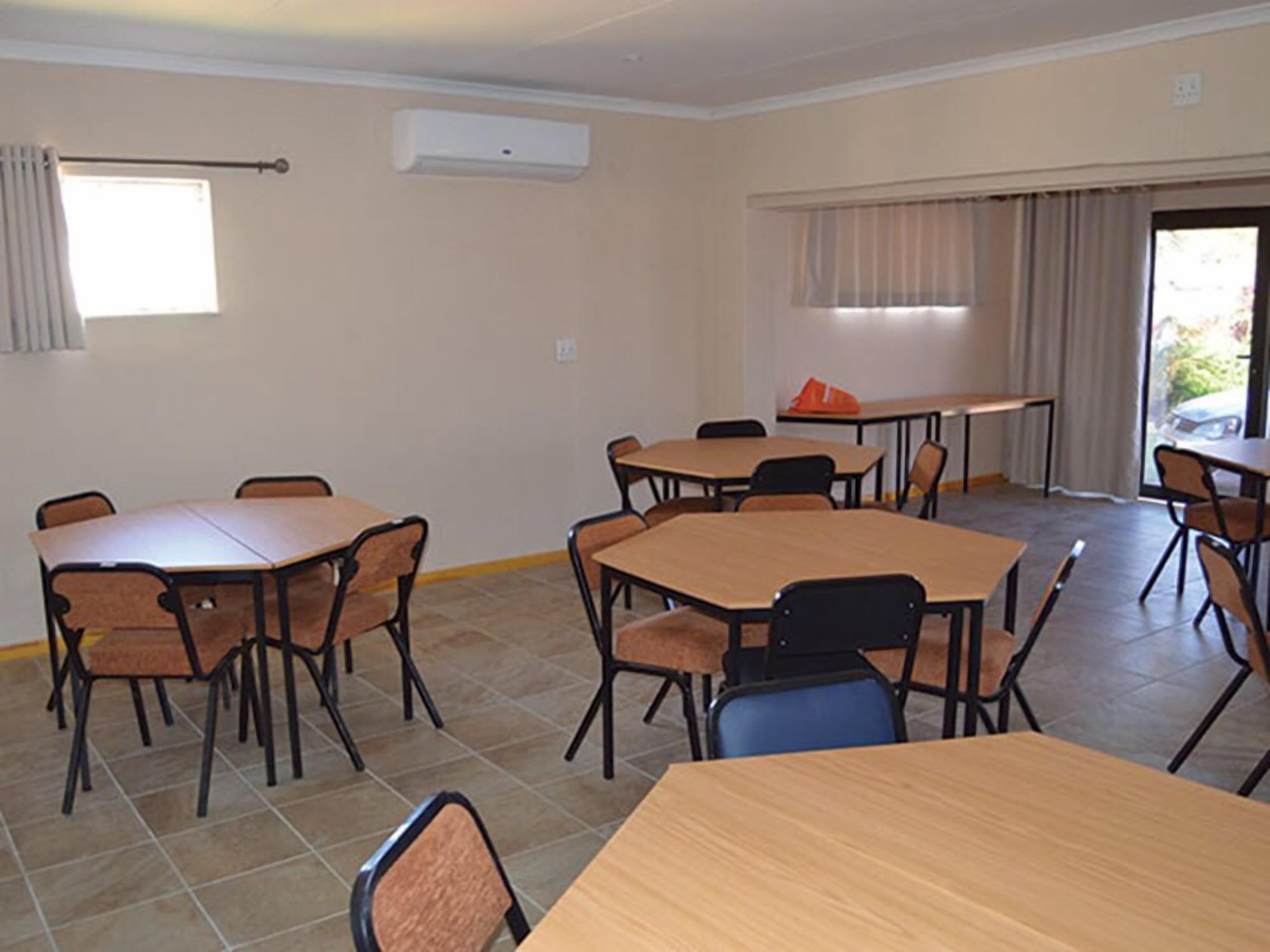 Une salle de conférence équipée de plusieurs tables et chaises, d’un système de climatisation et de fenêtres avec des rideaux.