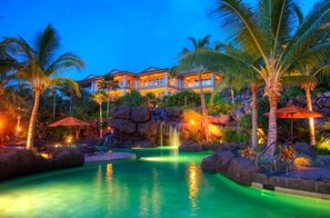 Un resort con piscina, palmeras y un edificio grande con múltiples balcones.