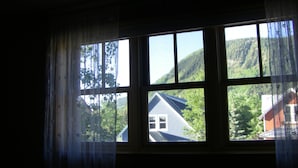 Une fenêtre donnant sur une maison et des montagnes.