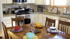Une cuisine avec des meubles blancs, des appareils en acier inoxydable et une table à manger en bois, accompagnée de chaises.