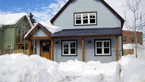 Une maison à deux étages, dotée d’un toit à pignon, d’un porche à l’avant et d’une allée recouverte de neige.