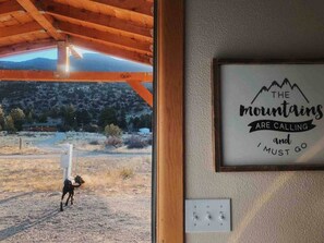 Un interior rústico con techo de madera, un letrero con una frase motivacional y vista a un perro afuera.