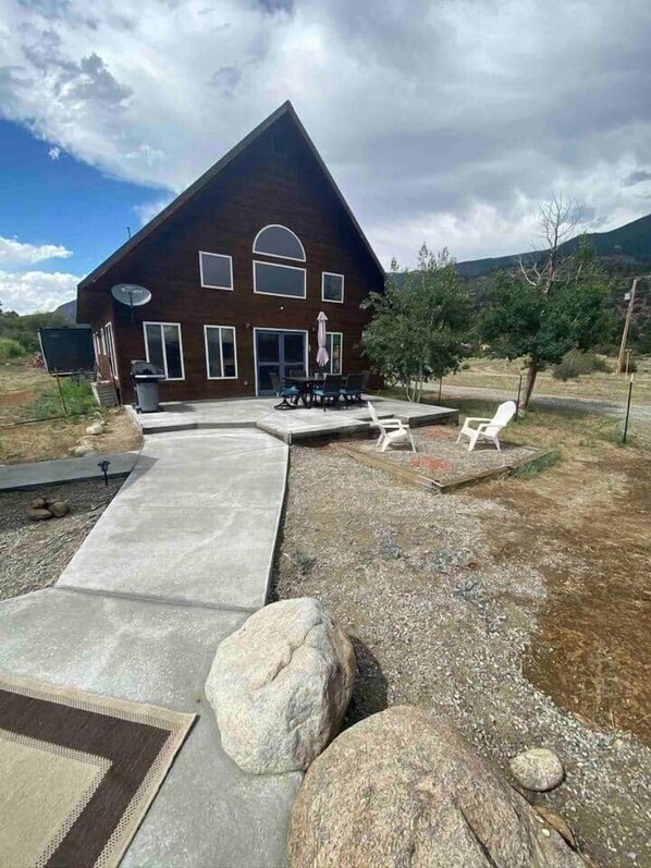 Casa de madera de dos pisos con un patio que incluye muebles de exterior y una antena parabólica.
