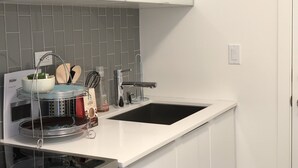 Una cocina moderna con armarios blancos, un lavamanos negro y una campana extractora de acero inoxidable.