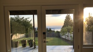 Vista a través de un ventanal de un jardín trasero con césped, plantas en macetas y una valla de madera.