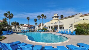 A pool area with blue lounge chairs, palm trees, and a building with a tower. - 1st FLOOR LARGE 1BR, BEAUTIFUL Beach Getaway!  Pool, Hot Tub, Sauna & More (Corpus Christi)
