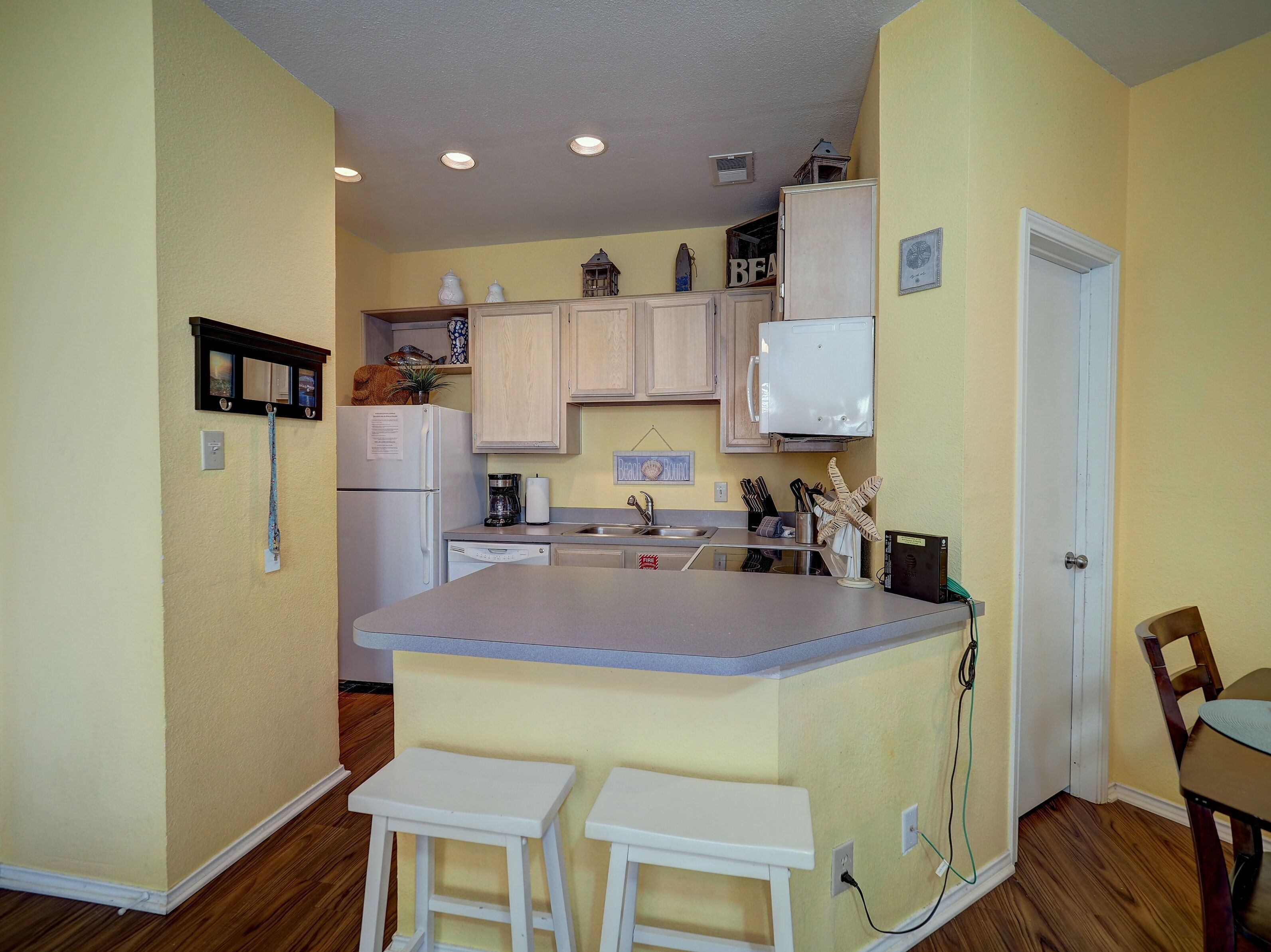 A compact kitchen with wooden cabinets, a white refrigerator, a built-in microwave, and a small island with stools.