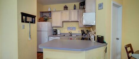 A compact kitchen with wooden cabinets, a white refrigerator, a built-in microwave, and a small island with stools.