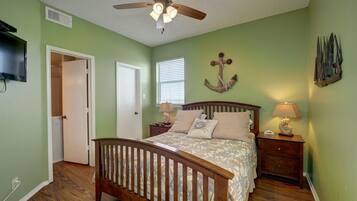 A bedroom with a wooden bed, a ceiling fan, a nightstand with a lamp, and a wall-mounted anchor decoration.