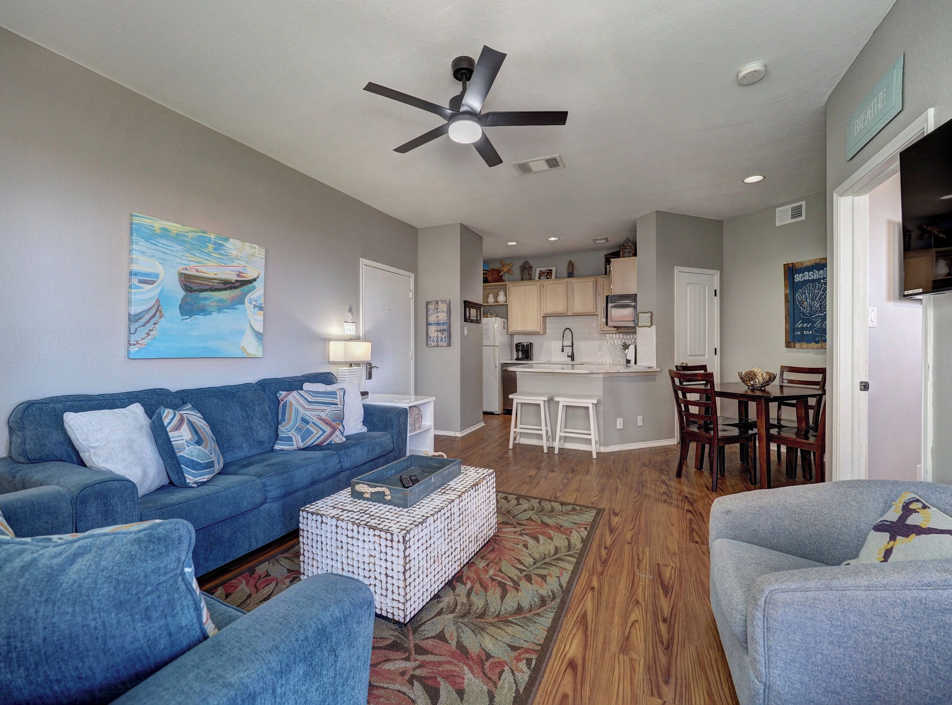 A living room with a blue sofa, a coffee table, and a ceiling fan.