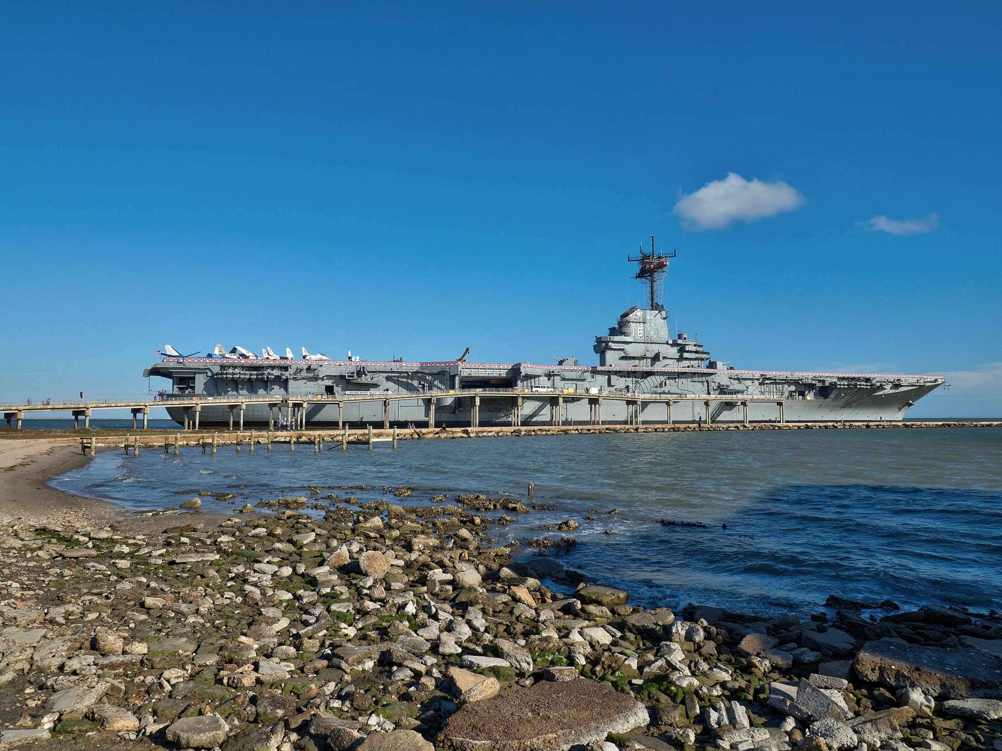 Un grand navire de guerre était amarré à un quai, avec une côte rocheuse en premier plan.