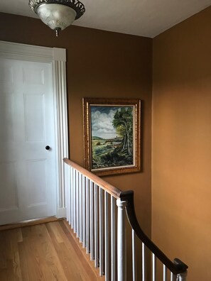 Stunning hallway with a framed landscape painting and a wooden handrail.