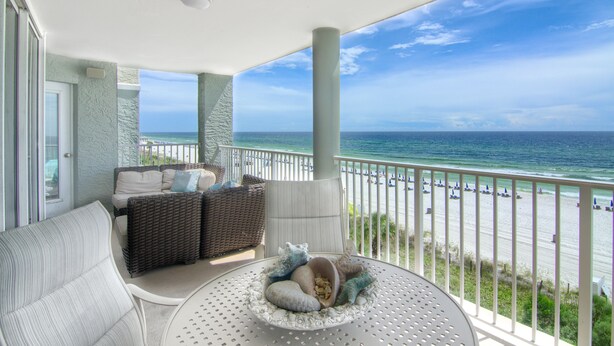 Un balcón con vistas a la playa, mobiliario de mimbre y una mesa redonda con un cuenco decorativo.