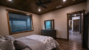 Um quarto com cama, cômoda, ventilador de teto e janela com persianas.