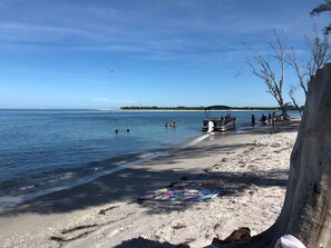 Une plage avec un bateau, des gens qui se baignent et un parasol de plage.