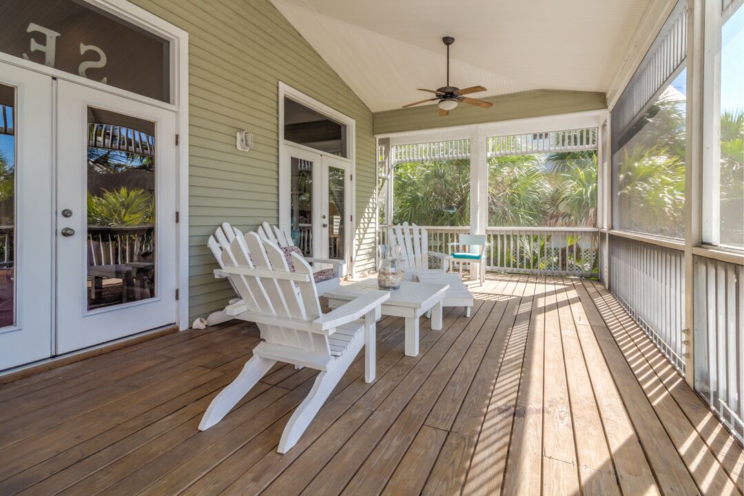 A covered porch with wooden flooring, white Adirondack chairs, and a ceiling fan.