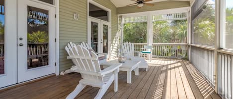 A covered porch with wooden flooring, white Adirondack chairs, and a ceiling fan.
