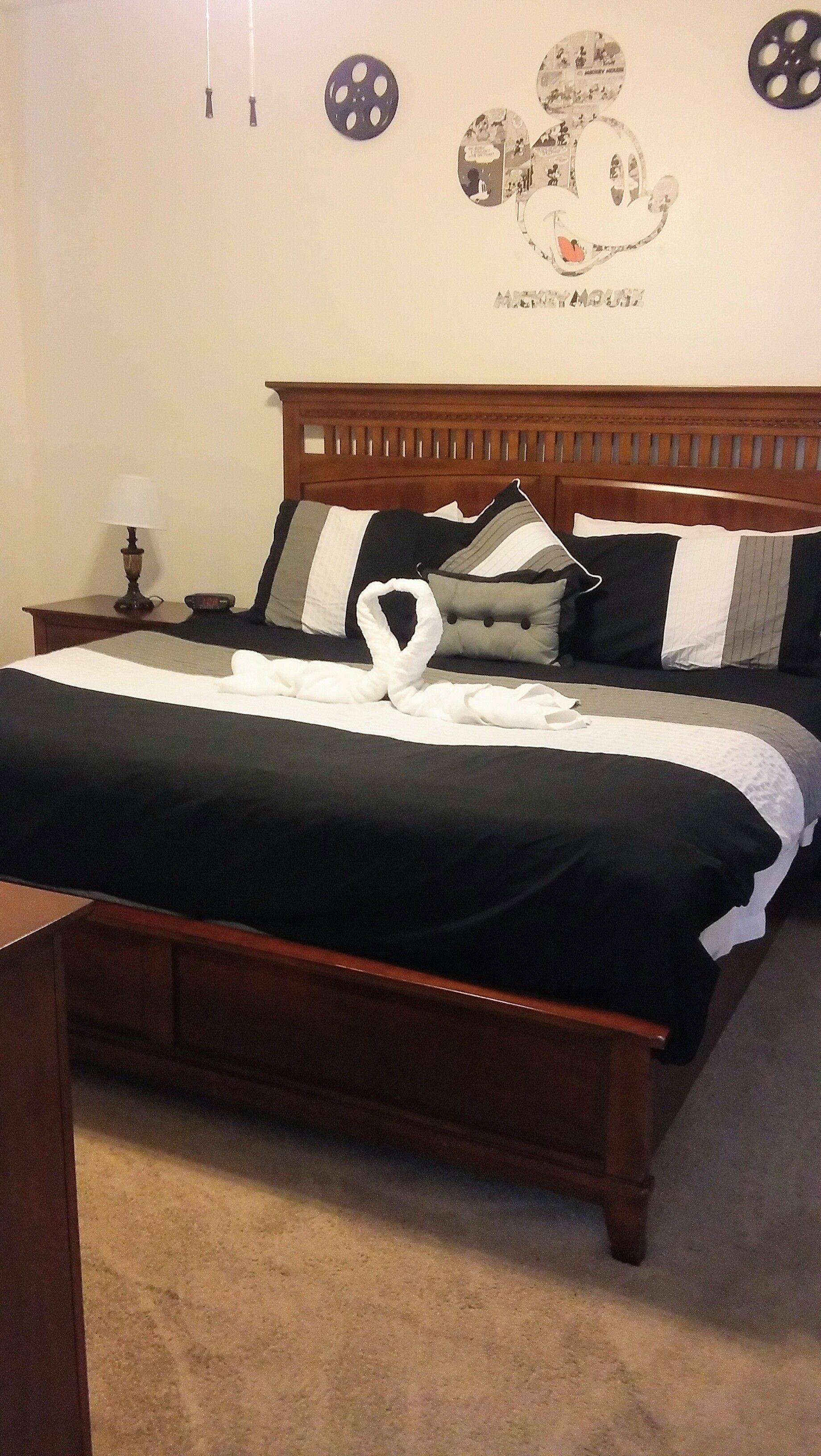 A neatly made bed with a black and white bedspread, a wooden headboard, and a wall decoration of Mickey Mouse.