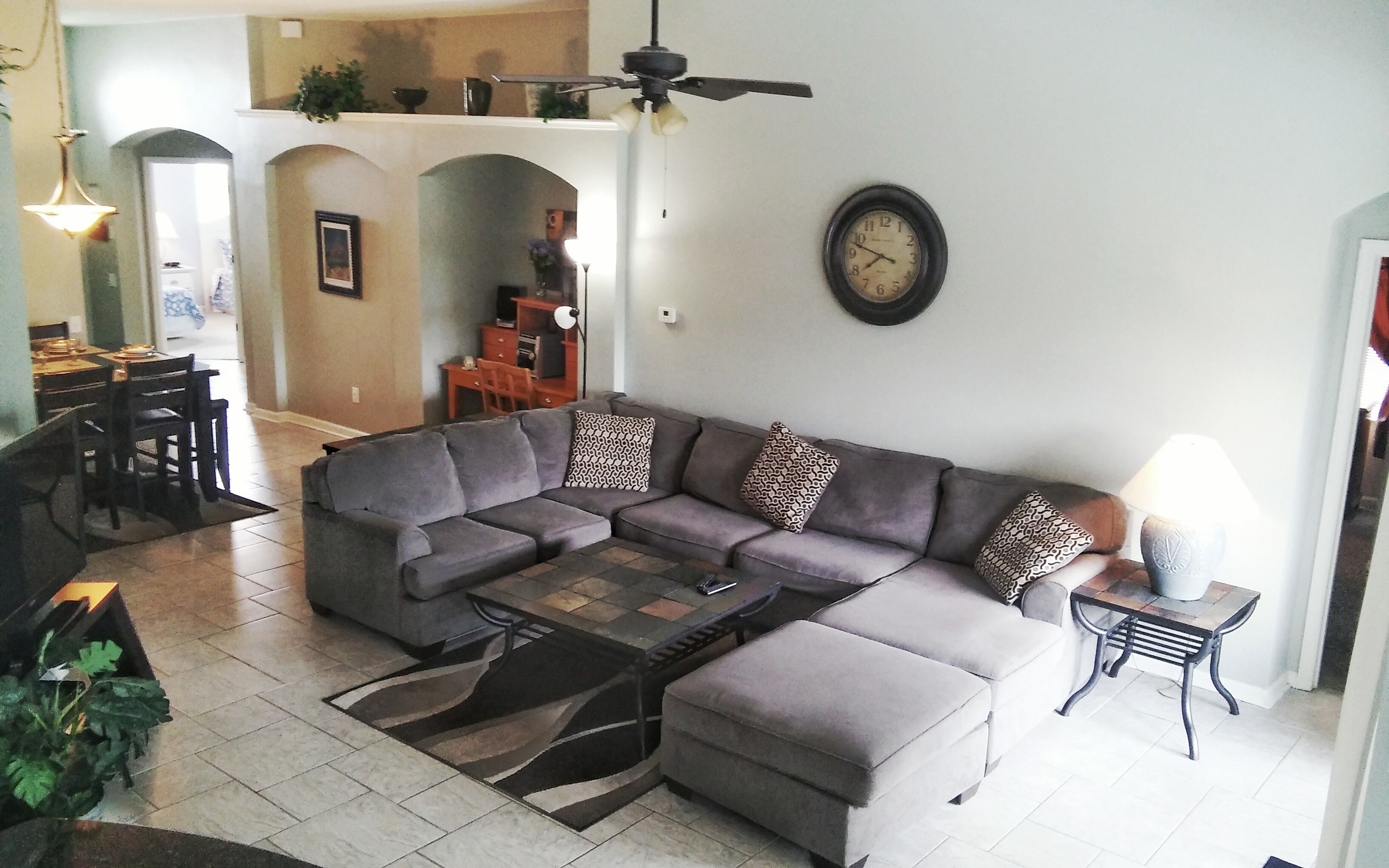 A living room with a sectional sofa, a coffee table, and a clock on the wall.