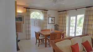 A dining area with a wooden table and chairs, a sofa with red cushions, and a window with curtains. - Sugar Hill - B8 by Island Villas (Holetown)