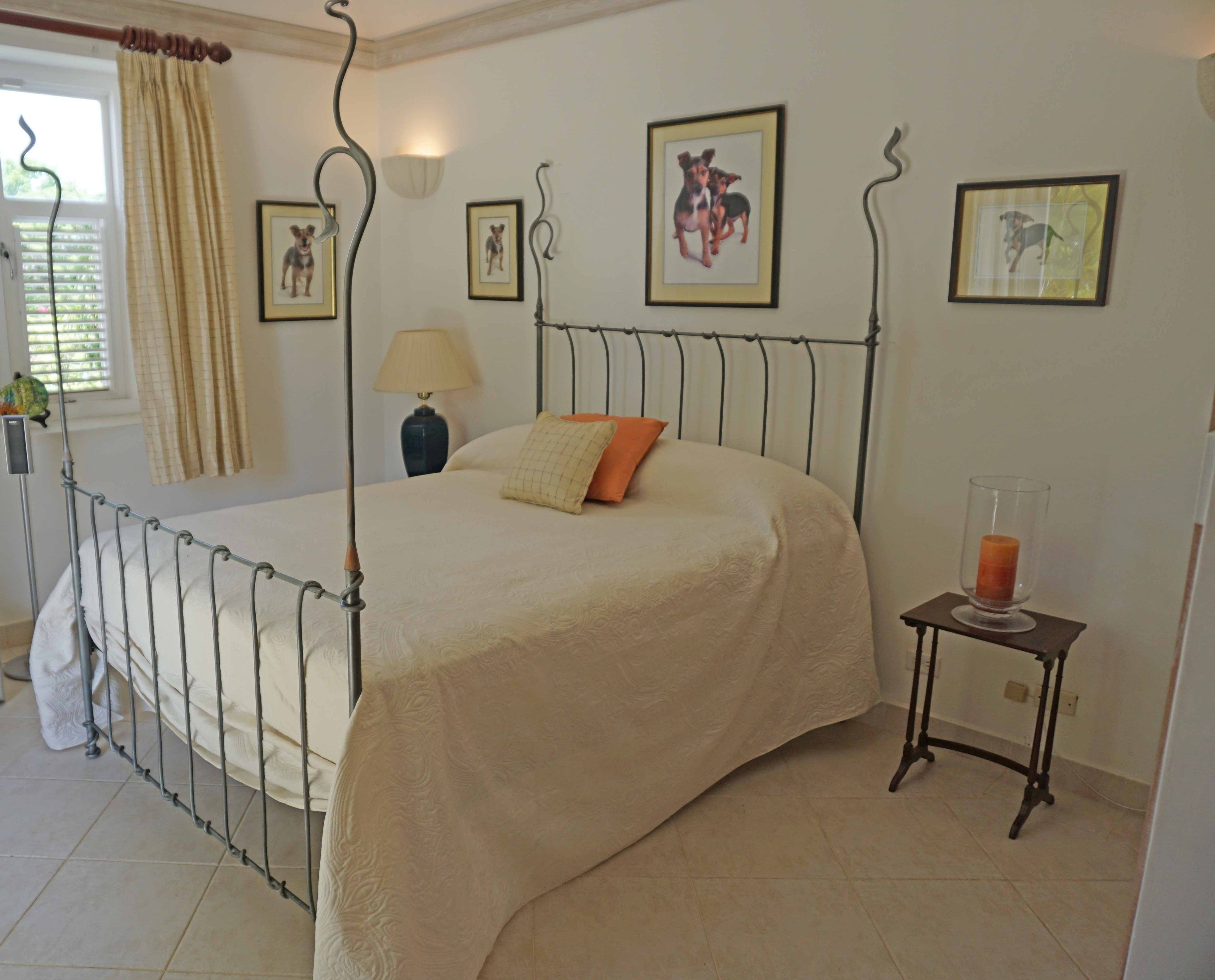 A bedroom with a metal bed frame, a bedside table with a lamp, and framed pictures on the wall.