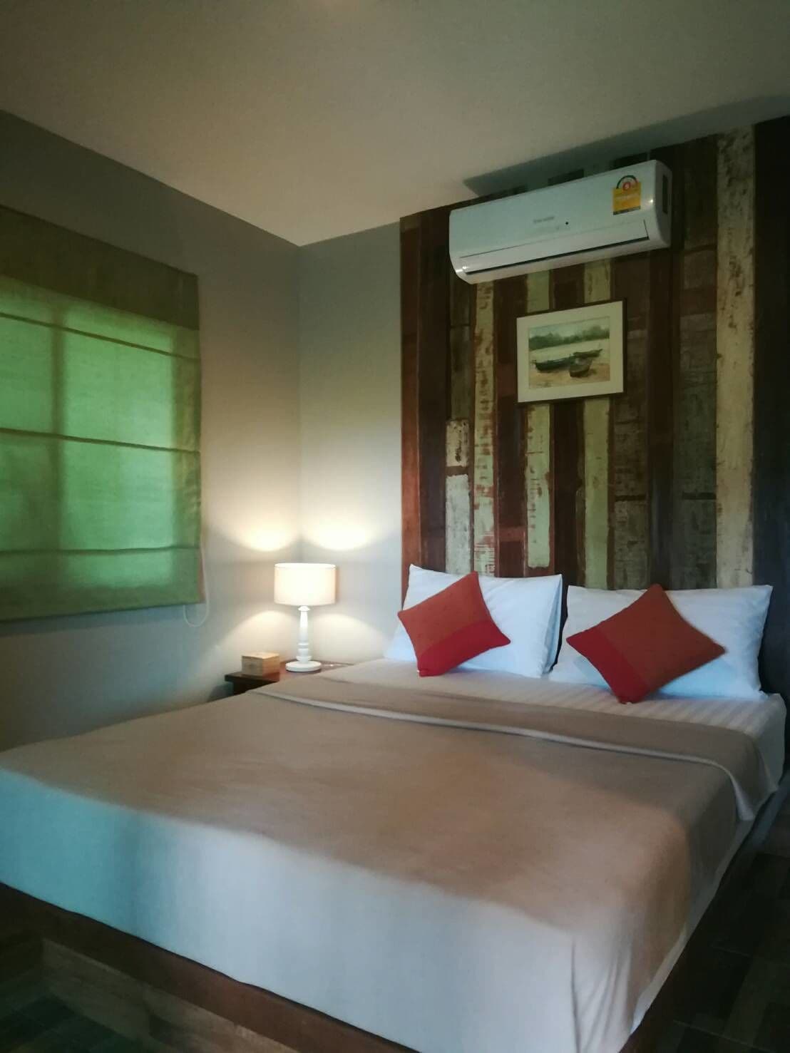 Una habitación de hotel con cama, mesita de noche, lámpara y aire acondicionado.