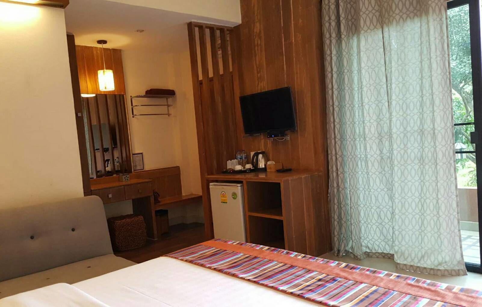 Una habitación de hotel con cama, escritorio, televisor y ventana con cortinas.