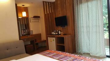 Una habitación de hotel con cama, escritorio, televisor y ventana con cortinas.